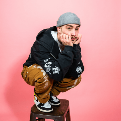 Person sitting on a stool against a pink background